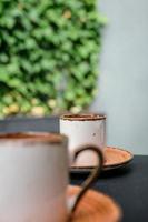 concentrez-vous sur l'autre côté de l'espresso. deux tasses de café mousseux noir turc sur une table en pierre noire avec des branches de lierre sauvage en arrière-plan, bizet à côté de la tasse. cadre vertical, mise au point sélective photo