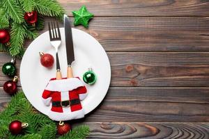 vue de dessus de la fourchette, du couteau et de l'assiette entourés de sapins et de décorations de noël sur fond en bois. concept de réveillon du nouvel an et de dîner de vacances photo