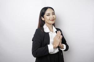 une jeune employée asiatique souriante portant un costume noir fait des gestes d'accueil traditionnels isolés sur fond blanc photo