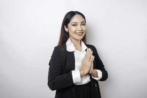 une jeune employée asiatique souriante portant un costume noir fait des gestes d'accueil traditionnels isolés sur fond blanc photo
