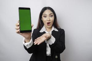 femme d'affaires asiatique surprise portant un costume noir montrant l'espace de copie sur son smartphone, isolée par fond blanc photo