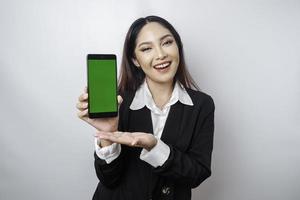 une jeune femme d'affaires heureuse porte un costume noir, montrant l'espace de copie sur son téléphone isolé par fond blanc photo