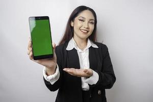 une jeune femme d'affaires heureuse porte un costume noir, montrant l'espace de copie sur son téléphone isolé par fond blanc photo