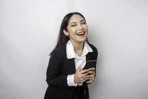 un portrait d'une femme d'affaires asiatique heureuse sourit et tient son smartphone portant un costume noir isolé par un fond blanc photo