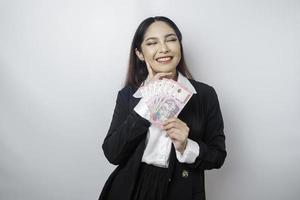 une jeune femme réfléchie porte un costume noir et tient de l'argent liquide en roupie indonésienne isolée par fond blanc photo