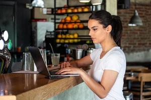 jeune femme avec un joli sourire assise avec un net-book portable dans un café moderne à l'intérieur pendant les heures de récréation, charmante étudiante heureuse utilisant un ordinateur portable pour se préparer au cours photo