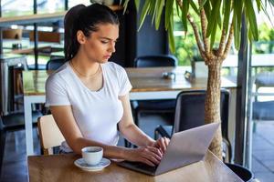 jeune femme avec un joli sourire assise avec un net-book portable dans un café moderne à l'intérieur pendant les heures de récréation, charmante étudiante heureuse utilisant un ordinateur portable pour se préparer au cours photo