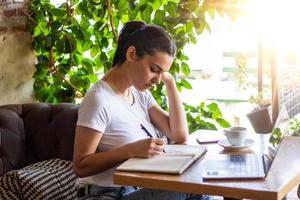 jeune femme avec un joli sourire assise avec un net-book portable dans un café moderne à l'intérieur pendant les heures de récréation, charmante étudiante heureuse utilisant un ordinateur portable pour se préparer au cours photo