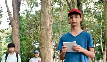 les garçons asiatiques à l'extérieur de la classe apprennent en notant les épices des arbres, des branches, des racines, du tronc et d'autres du jardin botanique à l'extérieur de la salle de classe avec des amis pendant le camp d'été, mise au point douce. photo