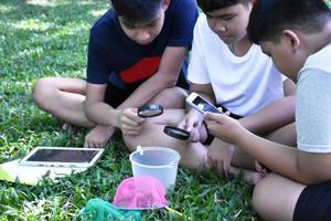 trois étudiants asiatiques tenant des loupes et d'autres dispositifs d'apprentissage, des tablettes, de petits filets de pêche et un petit bac en plastique blanc pour en savoir plus sur les insectes sous-marins après l'avoir sorti de l'étang. photo