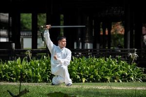 jeune homme pratiquant l'épée de tai chi traditionnelle, tai ji dans le parc pour un concept d'arts martiaux chinois traditionnels sains sur fond naturel. photo