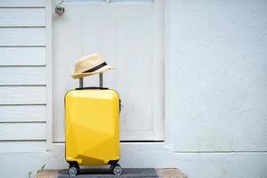 valise jaune, bagages avec chapeau à la porte d'entrée, départ de la maison pour des vacances et des vacances, voyage, préparez-vous pour l'aventure. photo