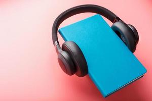 les écouteurs sont portés sur un livre dans une couverture rigide bleue sur fond rose, vue de dessus. photo