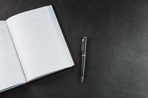 bureau avec un cahier ouvert noir et un stylo sur fond noir. photo