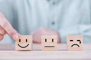 homme d'affaires choisit un sourire émoticône icônes visage heureux symbole sur bloc de bois , services et concept d'enquête de satisfaction client photo