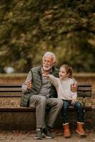 grand-père passe du temps avec sa petite-fille sur un banc dans le parc le jour de l'automne