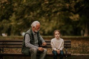 grand-père passe du temps avec sa petite-fille sur un banc dans le parc le jour de l'automne photo