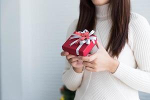 Femme en chandail tenant une petite boîte cadeau rouge sur fond blanc photo