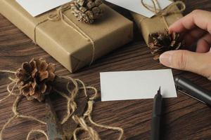 mains masculines emballant des cadeaux de nouvel an et écrivant des cartes sur une table en bois marron. photo