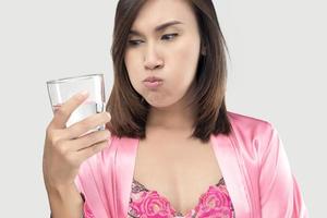 femme asiatique se rinçant et se gargarisant tout en utilisant un rince-bouche d'un verre sur fond gris. photo