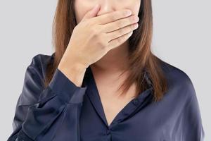 la femme en chemise bleu foncé ne commente pas et refuse. femme avec ses mains sur sa bouche à cause de la mauvaise haleine ou de l'halitose photo