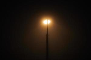 un lampadaire de nuit brille d'une faible lumière jaune mystérieuse à travers le brouillard du soir photo