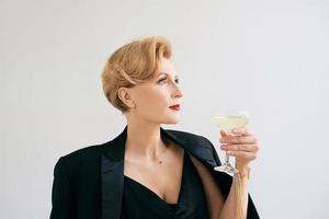 femme élégante et élégante mature en smoking avec un verre de vin mousseux. fête, célébration, concept anti-âge photo