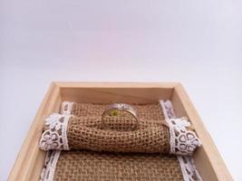 bague de mariage placée sur une boîte à bagues en bois avec une toile de jute comme base. avec fond blanc isolé photo