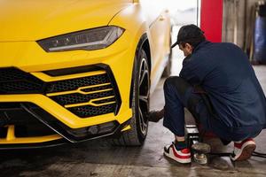 le mécanicien vérifie la pression des pneus dans la voiture de sport jaune suv. photo