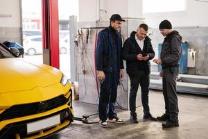 la mécanique et le directeur se tiennent contre le suv de voiture de sport jaune en réparation. photo