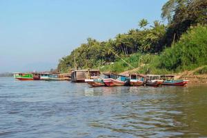 paysage tropical avec des bateaux à longue queue sur la rivière, des palmiers sur la rive et des montagnes à l'horizon. fleuve mékong, luang prabang, laos. photo