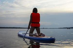 une adolescente nage sur une planche sup, une belle fille monte une planche avec une pagaie sur un beau lac, rivière photo