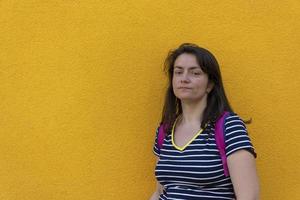 portrait d'une femme brune souriante avec un sac à dos, debout sur un fond jaune et regardant la caméra photo