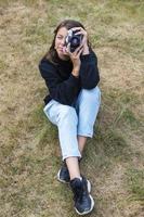 jolie adolescente avec un appareil photo, une fille prenant des photos sur un appareil photo vintage rétro sur l'herbe dans le parc, un concept de passe-temps