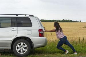 une voiture cassée. une jeune femme pousse une voiture cassée sur la route, une panne, sur fond de champ jaune photo