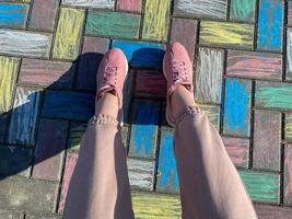 belles jambes féminines en baskets roses et pantalons à la mode sur fond de dalles en béton peintes avec des crayons lumineux colorés pour enfants joyeux photo