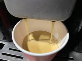 tasse à café en carton rouge dans laquelle un délicieux café americano noir chaud et revigorant est versé de la machine à café du bureau le matin photo