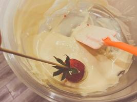 fraise sucrée en couches rouges trempée dans du beau chocolat belge fondu blanc avec des décorations sur un bâton. faire des fraises enrobées de chocolat photo