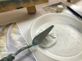 couteau à palette dans la main d'un artiste mélangeant des peintures acryliques de différentes couleurs dans une assiette bleue