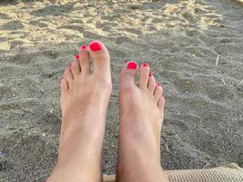 Jambes féminines, pieds avec une belle pédicure rouge sur fond de sable en vacances sur la plage dans un paradis tropical chaud de l'Est, station balnéaire du sud photo