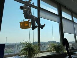 grimpeur nettoyer les fenêtres de l'extérieur du bâtiment en lavant le vitrage de la façade d'un immeuble à plusieurs étages