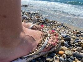 jambes féminines, pieds dans des pantoufles en caoutchouc avec une belle pédicure rouge sur fond de sable en vacances sur la plage dans un pays paradisiaque tropical chaud du sud photo