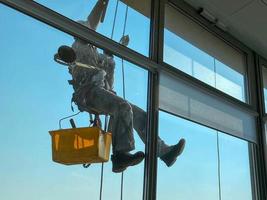 alpinisme industriel, un homme restaure les joints des fenêtres et les lave photo