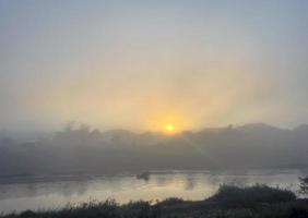 vue sur la rivière tôt le matin le soleil se lève de l'horizon à l'est. la douce lumière du soleil jaune doré frappe le brouillard et la vapeur. mise au point douce et sélective photo