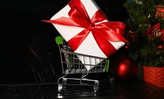 panier sur une carte d'ordinateur avec un énorme cadeau à côté de l'arbre de noël. shopping en ligne photo