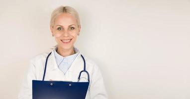 jeune femme médecin heureuse en manteau médical avec stéthoscope souriant avec tablette dans ses mains.copie espace bannière photo