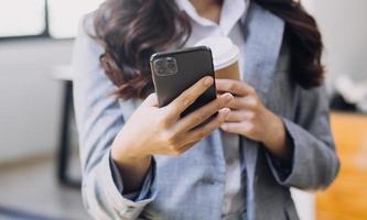 jeune femme d'affaires assise au bureau à table et utilisant un smartphone. sur le bureau se trouvent un ordinateur portable et une tablette, des graphiques et des graphiques à l'écran. femme analysant des données. étudiant apprenant en ligne. photo