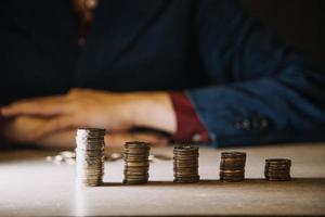 économiser de l'argent à la main en mettant des pièces sur la pile sur la table avec le soleil. concept finance et comptabilité photo