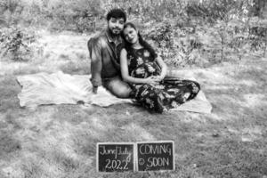 couple indien posant pour une séance photo de maternité. le couple pose dans une pelouse avec de l'herbe verte et la femme étale sa bosse de bébé dans le jardin de lodhi à new delhi, inde - noir et blanc