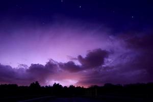 la foudre frappe à travers les nuages d'orage illuminant le ciel nocturne. photo